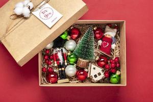 handgemachtes pflegepaket, saisonale geschenkbox mit spielzeug, weihnachtsdekor auf rotem tisch personalisierter umweltfreundlicher korb für familie, freunde, mädchen für den 24. dezember, weihnachten, neujahrstag flach gelegt foto