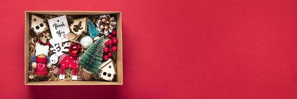 handgemachtes pflegepaket, saisonale geschenkbox mit spielzeug, weihnachtsdekor auf rotem tisch personalisierter umweltfreundlicher korb für familie, freunde, mädchen für den 24. dezember, weihnachten, neujahrstag flach gelegt foto