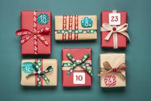 handgemacht verpackte rote, grüne geschenkboxen verziert mit bändern, schneeflocken und zahlen, weihnachtsdekorationen und dekor auf grünem tisch xmas adventskalender konzept draufsicht flach legen feiertagskarte foto