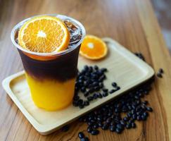 Eiskaffee-Getränkekarte Orange Americano mit frischen Orangenfrüchten, gemischt in einem Plastikbecher auf der Holztheke im Café foto