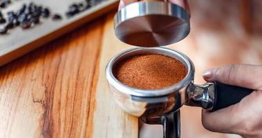 Nahaufnahme des Handbarista-Cafés, das Kaffee mit manuellen Pressen gemahlenen Kaffee mit Tamper auf der hölzernen Thekenleiste im Café zubereitet foto