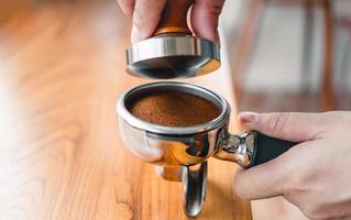 Nahaufnahme des Handbarista-Cafés, das Kaffee mit manuellen Pressen gemahlenen Kaffee mit Tamper auf der hölzernen Thekenleiste im Café zubereitet foto