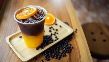 Eiskaffee-Getränkekarte Orange Americano mit frischen Orangenfrüchten, gemischt in einem Plastikbecher auf der Holztheke im Café foto