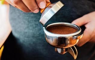 Nahaufnahme des Hand-Barista-Cafés, das Kaffee mit manuellen Pressen gemahlenen Kaffee mit Tamper im Café zubereitet foto