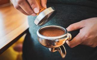 Nahaufnahme des Hand-Barista-Cafés, das Kaffee mit manuellen Pressen gemahlenen Kaffee mit Tamper im Café zubereitet foto