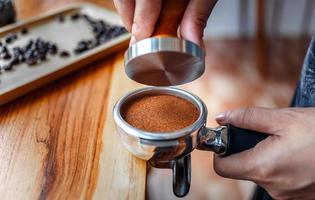 Nahaufnahme des Handbarista-Cafés, das Kaffee mit manuellen Pressen gemahlenen Kaffee mit Tamper auf der hölzernen Thekenleiste im Café zubereitet foto