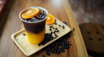 Eiskaffee-Getränkekarte Orange Americano mit frischen Orangenfrüchten, gemischt in einem Plastikbecher auf der Holztheke im Café foto