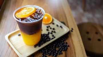 Eiskaffee-Getränkekarte Orange Americano mit frischen Orangenfrüchten, gemischt in einem Plastikbecher auf der Holztheke im Café foto