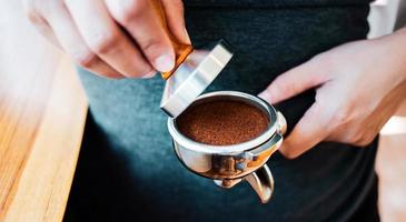 Nahaufnahme des Hand-Barista-Cafés, das Kaffee mit manuellen Pressen gemahlenen Kaffee mit Tamper im Café zubereitet foto