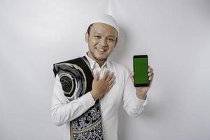 ein Porträt eines glücklichen asiatischen muslimischen Mannes, der lächelt, während er Kopienraum auf seinem Telefon zeigt, isoliert durch weißen Hintergrund foto