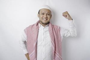 Aufgeregter asiatischer muslimischer Mann, der eine starke Geste zeigt, indem er seine Arme und Muskeln stolz lächelt foto