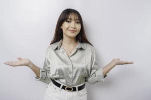 Aufgeregte asiatische Frau mit salbeigrünem Hemd, die auf den Kopierbereich neben ihr zeigt, isoliert durch weißen Hintergrund foto