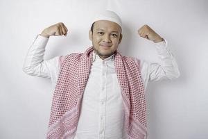Aufgeregter asiatischer muslimischer Mann, der eine starke Geste zeigt, indem er seine Arme und Muskeln stolz lächelt foto