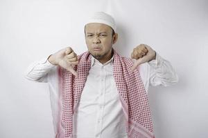 enttäuschter asiatischer muslimischer Mann gibt Daumen nach unten Handgeste der Zustimmung, isoliert durch weißen Hintergrund foto
