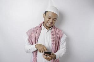 ein Porträt eines glücklichen asiatischen muslimischen Mannes, der lächelt, während er sein Telefon hält, isoliert durch weißen Hintergrund foto