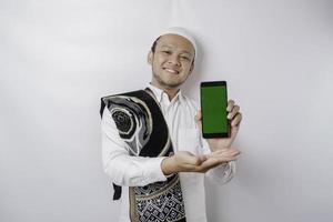 ein Porträt eines glücklichen asiatischen muslimischen Mannes, der lächelt, während er Kopienraum auf seinem Telefon zeigt, isoliert durch weißen Hintergrund foto
