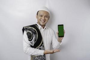 ein Porträt eines glücklichen asiatischen muslimischen Mannes, der lächelt, während er Kopienraum auf seinem Telefon zeigt, isoliert durch weißen Hintergrund foto