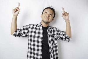 Der lächelnde asiatische Mann mit Tartanhemd zeigt auf den Kopierbereich auf ihm, isoliert durch weißen Hintergrund foto