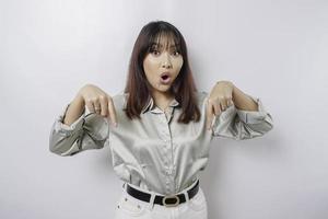 schockierte asiatische Frau mit salbeigrünem Hemd, die auf den Kopierbereich unter ihr zeigt, isoliert durch weißen Hintergrund foto