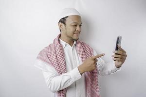 ein Porträt eines glücklichen asiatischen muslimischen Mannes, der lächelt, während er sein Telefon hält, isoliert durch weißen Hintergrund foto