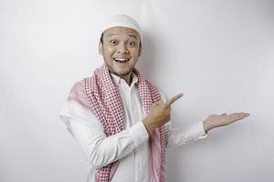 Aufgeregter asiatischer muslimischer Mann, der auf den Kopierbereich neben ihm zeigt, isoliert durch weißen Hintergrund foto