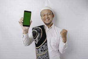ein glücklicher junger asiatischer muslimischer mann mit einem erfolgreichen ausdruck, der kopienraum auf seinem telefon zeigt, das durch weißen hintergrund isoliert wird foto