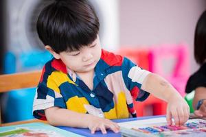 Porträt 3-jähriger asiatischer Junge ist dabei, Kunst zu machen. Kind hebt Buntstifte auf. Kunststunde. Schule zu Hause. foto