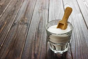 Weißer Kristallzucker in weißer Tasse mit Holzlöffel auf Holzhintergrund foto