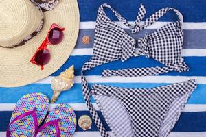 Badeanzug mit Strandzubehör auf blauem Hintergrund. Sonnenbrille Draufsicht Muschel Shorts Flip Flops Badeanzug foto