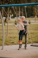 großvater verbringt am herbsttag zeit mit seiner enkelin auf dem parkspielplatz foto