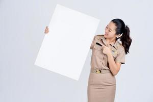 schöne asiatische Frau in brauner Uniform, die leere weiße Plakatwand isoliert auf weißem Hintergrund zeigt und hält. foto