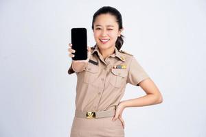 Schöne asiatische Frau in brauner Arbeitskleidung, die ein Smartphone-Modell mit leerem Bildschirm auf weißem Hintergrund hält. foto