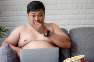 Der dicke Mann ist schockiert, als er zu Hause einen Film auf einem Laptop mit Popcorn ansieht. foto