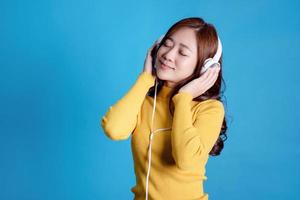 schöne frauen tragen gelbe freizeitkleidung. sie hört gerne musik mit kopfhörern auf hellblauem hintergrund. foto