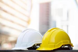 gelb-weißer Helmhut mit harter Schutzkleidung im Projekt auf Baustellengebäude auf Betonboden in der Stadt mit Sonnenlicht. Helm für Arbeiter als Ingenieur oder Arbeiter. Konzept Sicherheit zuerst.