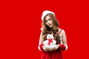 asiatische Teenager-Mädchen, die als Weihnachtsmann verkleidet sind und einen roten Hintergrund des Teddybären halten. Weihnachtskonzept. foto