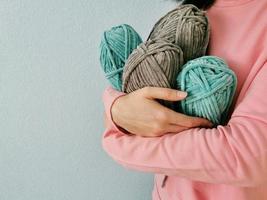 Frau, die in ihren Händen Stränge aus blauem und grauem Plüschstrickgarn auf blauem Hintergrund hält. Garn zum Stricken von Spielzeug, Kinder- und Erwachsenenkleidung, Einrichtungsgegenständen. handgemachtes Hobby. Seitenansicht aus nächster Nähe. foto