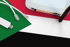 sudan-flagge auf dem tisch mit internet-rj45-kabel, drahtlosem usb-wlan-adapter und router. Konzept der Internetverbindung foto