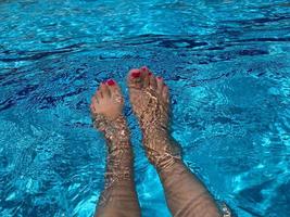 schöne frauenbeine im blauen wasser. schöne weibliche füße, die sich am schwimmbad entspannen. Sommerhintergrund für unterwegs foto