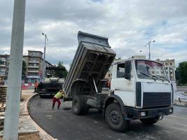 Straßenbauarbeiter reparieren Autobahn an sonnigen Sommertagen. Lader und Lastwagen auf neu hergestelltem Asphalt. schwere maschinen, die auf der straße arbeiten. Bordsteine, die mit Kies gebaut werden foto