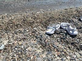 Urlaubshintergrund mit hellen Flip-Flops am Meereskieselstrand, Draufsicht foto