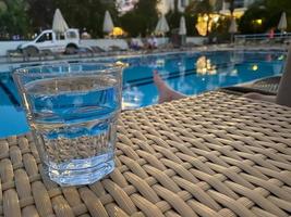 Weißes Gewinnglas mit Blumen vor einem Swimmingpool foto