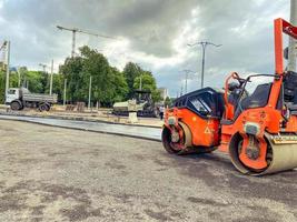 Bau neuer Gebäude und Strukturen, hohe Häuser für das Leben der Menschen. Asphaltstraßenbau. Orange Maschine verdichtet Beton. Asphaltfertiger bei der Arbeit foto