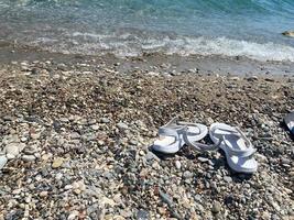 Flip-Flops an einem Sandstrand mit Meerwasser, das an Land gespült wird, und Muscheln. sommerferienkonzept foto