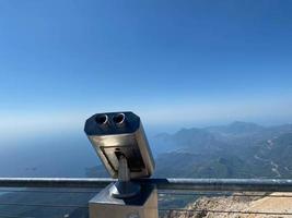 metallgraues stationäres Fernglas auf der Aussichtsplattform mit Blick auf das Meer, die Berge und die Stadt. Meereslandschaft von der hohen Küste foto