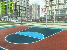 Outdoor-Sportarten. Basketballplatz in einem Wohngebiet. Ballspiel neben hohen Glashäusern. auf der Baustelle eine zuverlässige rutschhemmende Gummierung foto