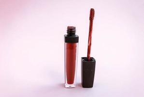 Bürste für Make-up-Lippen über der Flasche mit flüssigem Lippenstift, Nahaufnahme auf rosafarbenem Hintergrund mit Copyspace foto