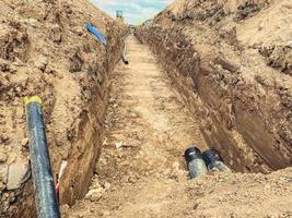 Bau eines neuen Quartiers. Graben eines Grabens zum Verlegen von Abwasserrohren. Kanalisation in Wohngebäuden. breite schwarze Rohre im Boden foto