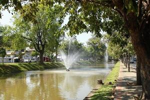 Blick auf einen Kanal mit Springbrunnen, großen Bäumen und Straßen am Ufer. Chiang Mai, Thailand. foto