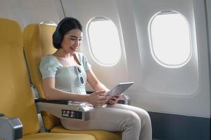 Junge Frau, die während des Fluges in der First-Class-Kabine Lieblingslieder mit mobiler Wiedergabeliste und Zubehör hört, Frau, die an Bord des Flugzeugs Musik über Kopfhörer vom Smartphone genießt foto